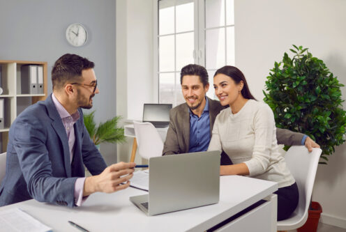 Happy couple sitting with a business broker or insurance agent showing project on a laptop screen